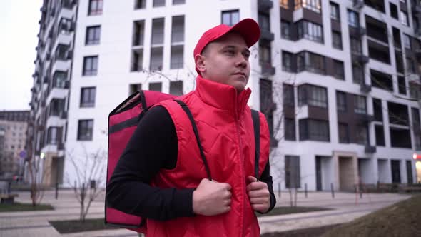 Delivery Guy Wearing Red Uniform While Walking Along Modern Buildings Down City Street with Thermal