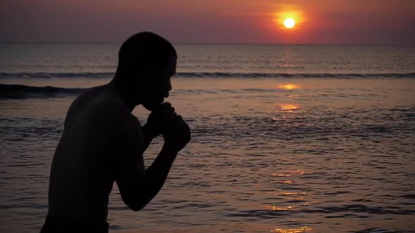 Young boxer trains on the beach of sea over sunset slow motion