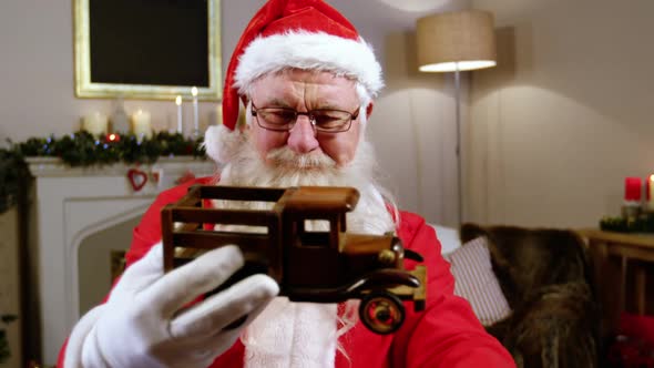 Santa claus holding and looking at a toy car alt