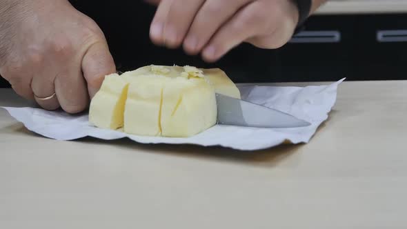 A Man's Hand of a Chef with a Large Knife Cuts Butter Into Many Pieces
