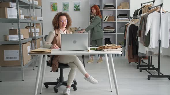 Beautiful Young Woman Working in a Clothing Store Selling Goods Online with a Female Colleague alt