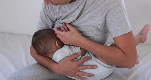 Young mother breastfeeding her baby at home sitting on bed alt