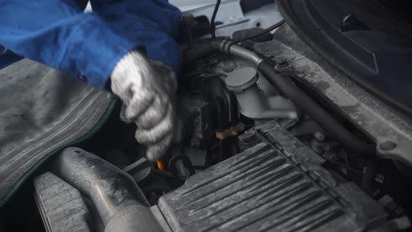 Hand of worker is woman holding oil dipstick checking oil level in engine of car in the garage. alt