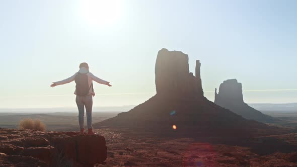 Woman Traveller with Arms Raised on Top of Mountain Looking at Monument Valley alt