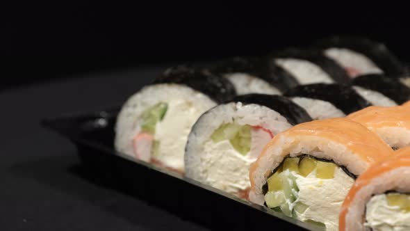 Sushi Rolls Rotates in a Plastic Container on a Black Background. Meal Delivery alt