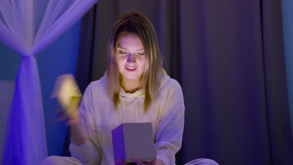 Surprised Smiling Woman Opens Golden Glitter Gift Box with Magic Light Inside 8K alt