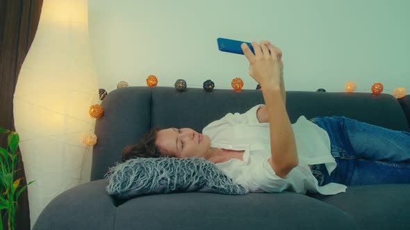 Portrait of a Young Woman Lying on the Sofa and Making Selfie Photo While Kissing at Camera alt