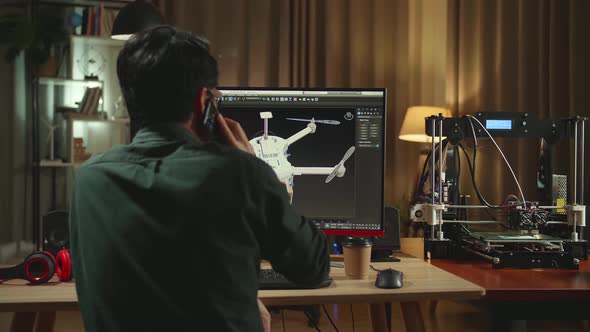 Back View Of Asian Engineer Talking On Mobile Phone While Work On Personal Computer And 3D Printer alt
