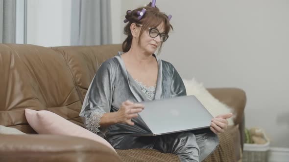 Portrait of Tired Senior Woman Closing Laptop and Leaning Back on Couch at Home alt