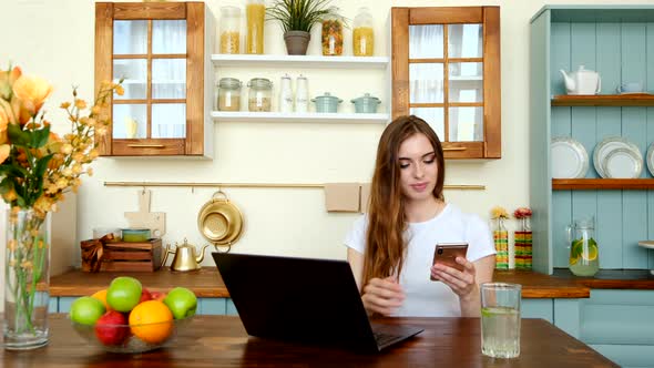 Young Serious Woman Sitting In The Kitchen And Working Online From Home
