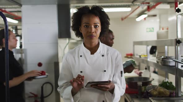 Portrait of african american female chef holding tablet looking at camera and smiling alt