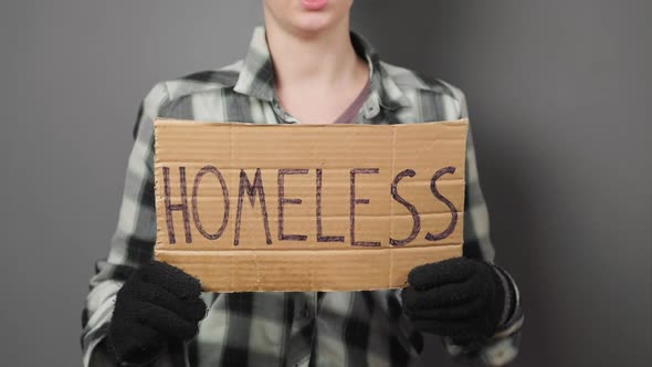 A untidy beggar woman holds a cardboard sign with the inscription homeless. alt