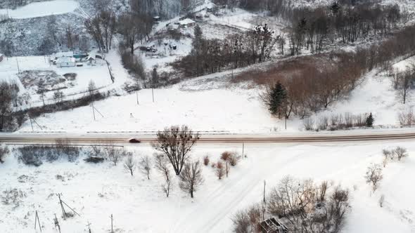 The Car Drives Along a Flat Road in Winter Among the Village  Aerial Side View alt