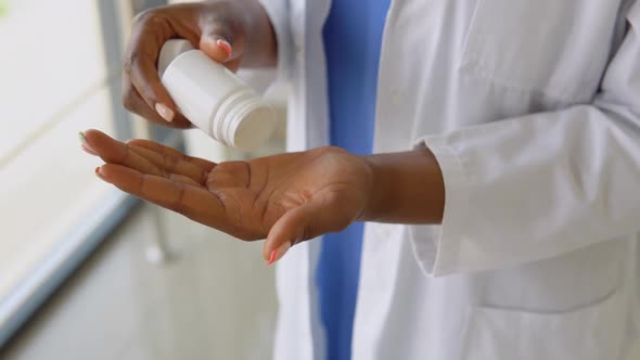 African American Doctor Woman in a Blue Suit and White Coat Pours Pills From a Jar on Her Palm alt