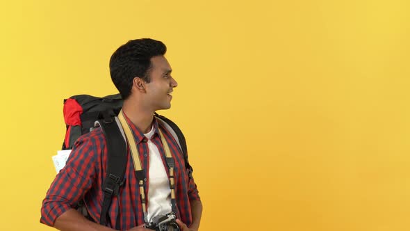 Surprised young Indian tourist man doing open hand gesture to empty space aside on yellow background
