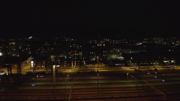 Drone shot of empty railways depot and cars drive on city street at night. alt