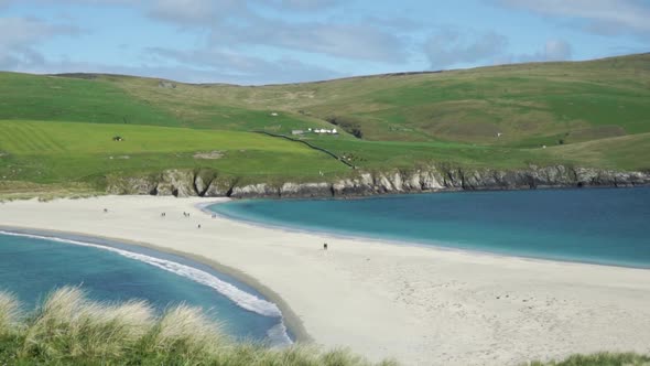 People crossing the St Ninian's Isle sand bar at low tide on a clear day alt