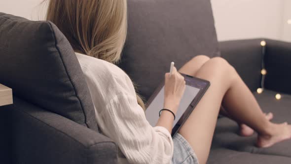 Young Asian woman in white shirt sitting on the sofa and using tablet.