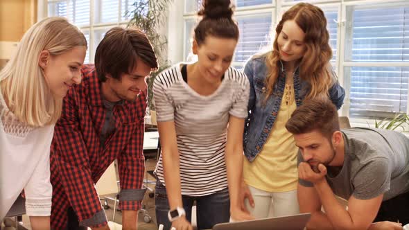Group of business executives discussing over laptop at their desk alt