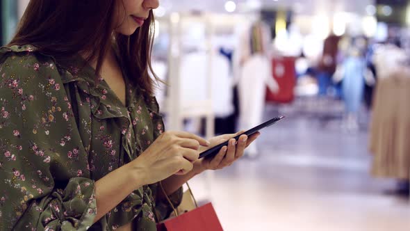 Young asian woman with shopping bags using smart phone and shopping at mall