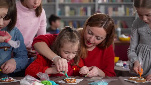 Woman Helping Autistic Girl Icing Cookie in Class alt