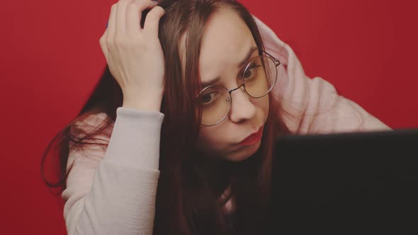Young Woman in Glasses Works on Laptop and Scratches Head Sitting in Home Office alt
