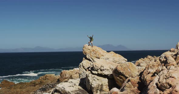 African american man hiking raising hands standing on rock by the sea alt