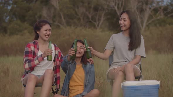 Asian woman sitting on a chair with friends camping in nature having fun together drinking beer.