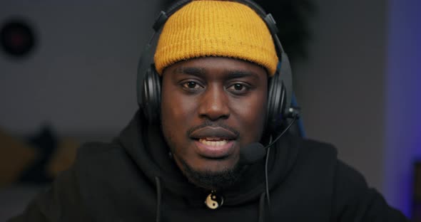 A Serious Man in a Yellow Cap with a Headset Carefully Plays a Video Shooter on Computer alt