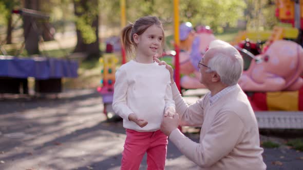 Grandfather having fun with his cute little granddaughter in the amusement park