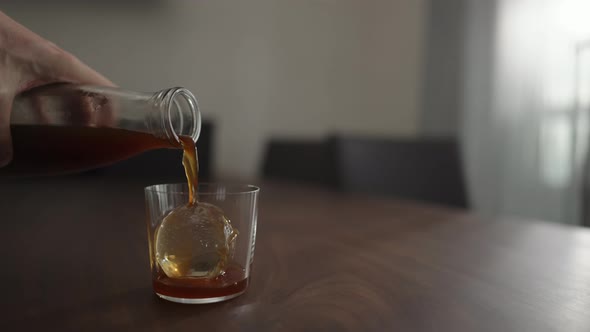 Slow Motion Pour Cold Brew Coffee Over Ice Ball in Tumbler Glass on Walnut Table alt