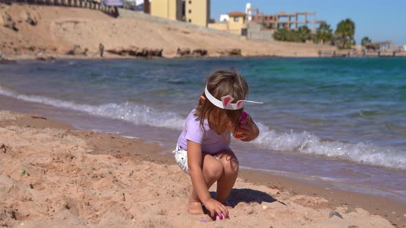 Happy Girl Playing with Easter Eggs on the Beach