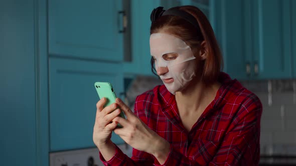 Young 30s Woman with White Cosmetic Mask on Her Face Using Mobile Phone, Making Grimace for Selfie