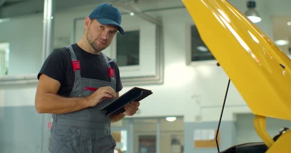 In a Garage a Mechanic Using the Tablet Makes the Oil and Engine Check To the Car Smiles. Concept Of alt