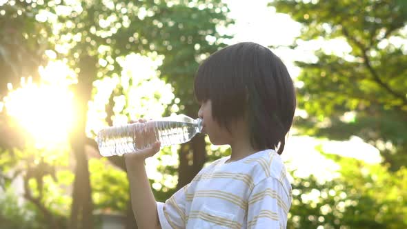 Cute Asian Boy Drinking Water From A Bottle In The Park alt
