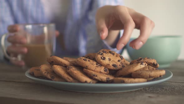 The Girl Drinks Coffee And Eats Cookies. Lots Of Chocolate Chip Cookies On A Gray Plate. alt