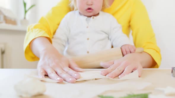 A little happy girl and her mom are rolling out cookie dough with a rolling pin alt