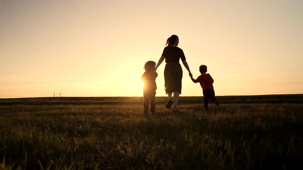 Silhouette of Young Family Mom and Two Brothers Twins Boys Runs to the Sun on Open Air Field or Park alt