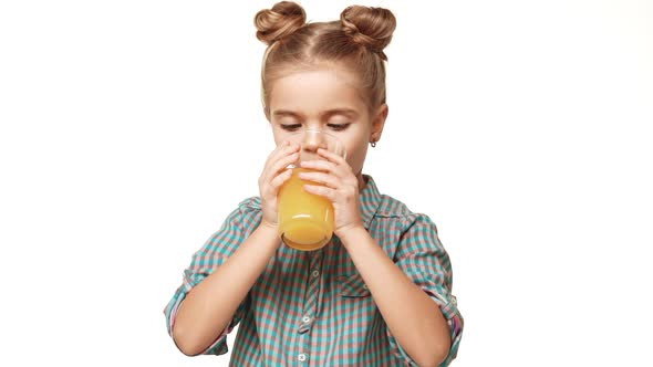 Cute Small Caucasian Girl Kid in Plaid Shirt and Hair Buns Drinking Orange Juice From Glass and alt