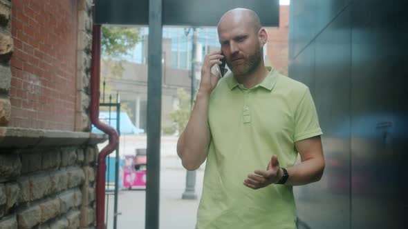 Serious Young Man Speaking on Mobile Phone Walking Outdoors in Urban Street alt