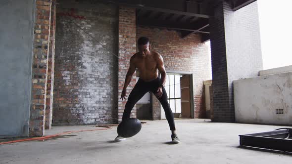 Shirtless african american man exercising with medicine ball in an empty urban building alt