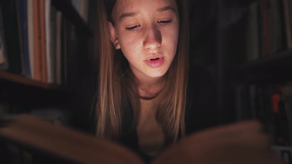 Girl in Library Between the Bookshelves and Reading Book Aloud for Finding Information alt