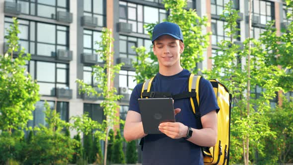 Smiling Delivery Man Courier with Thermal Bag Uses Tablet Confirm Client Order alt
