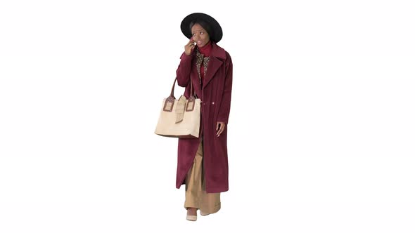 African American Fashion Girl in Coat and Black Hat Talking on the Phone While Walking on White alt
