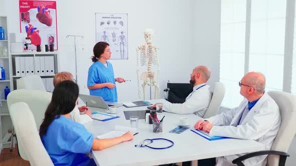 Assistent Pointing on Skeleton in Front of Medical Stuff alt
