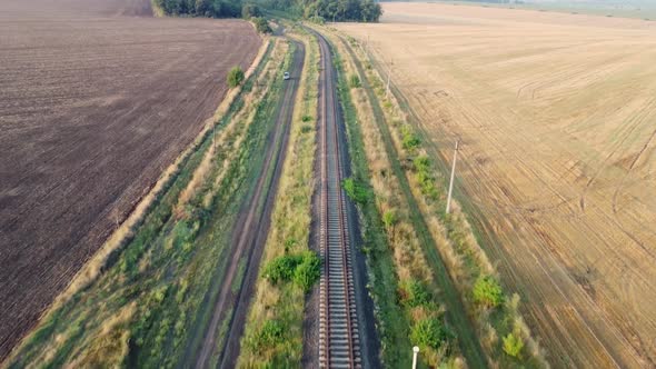 Railway through fields and forests. A small car on a dirt road alt