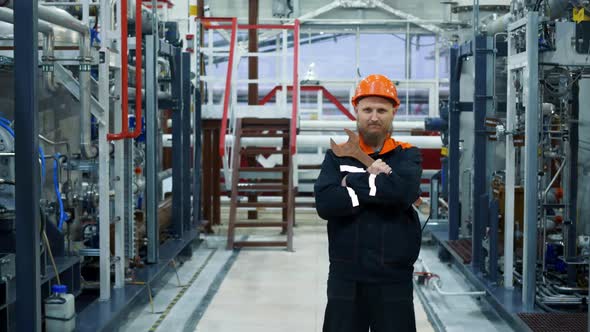 A Bearded Male Mechanic in an Orange Helmet with a Large Wrench Stands in a Fuel Gas Preparation alt