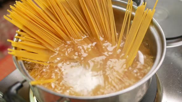 Raw spaghetti is being cooked in boiling water in a kitchen pot. alt