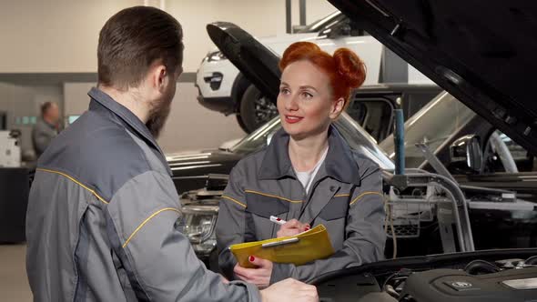 Lovely Female Mechanic Taking Notes, Talking To a Colleague at the Garage alt