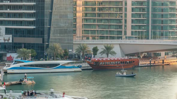 Yachts and Boats with Tourists Staying Near Shoping Mall and Passing Under a Bridge in Dubai Marina alt